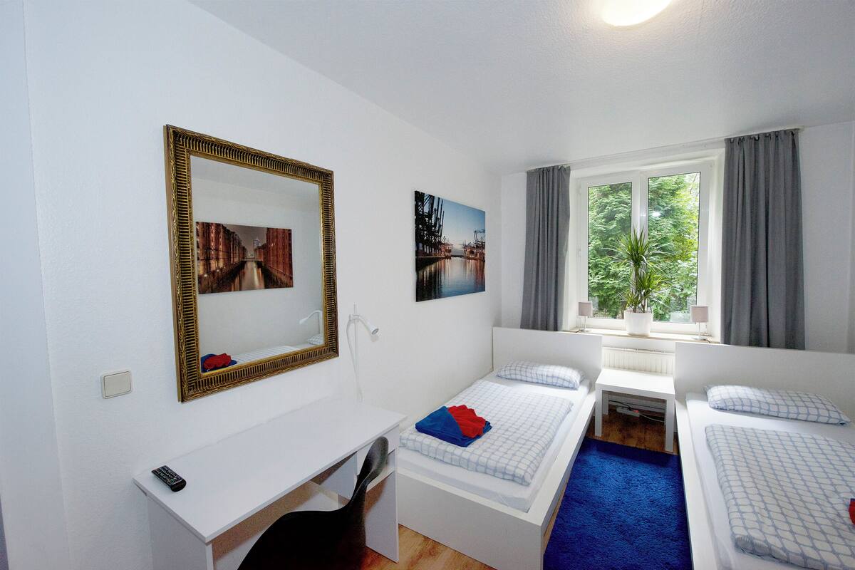 A hotel room with a bed, a desk, a chair, a mirror, and a window with curtains.