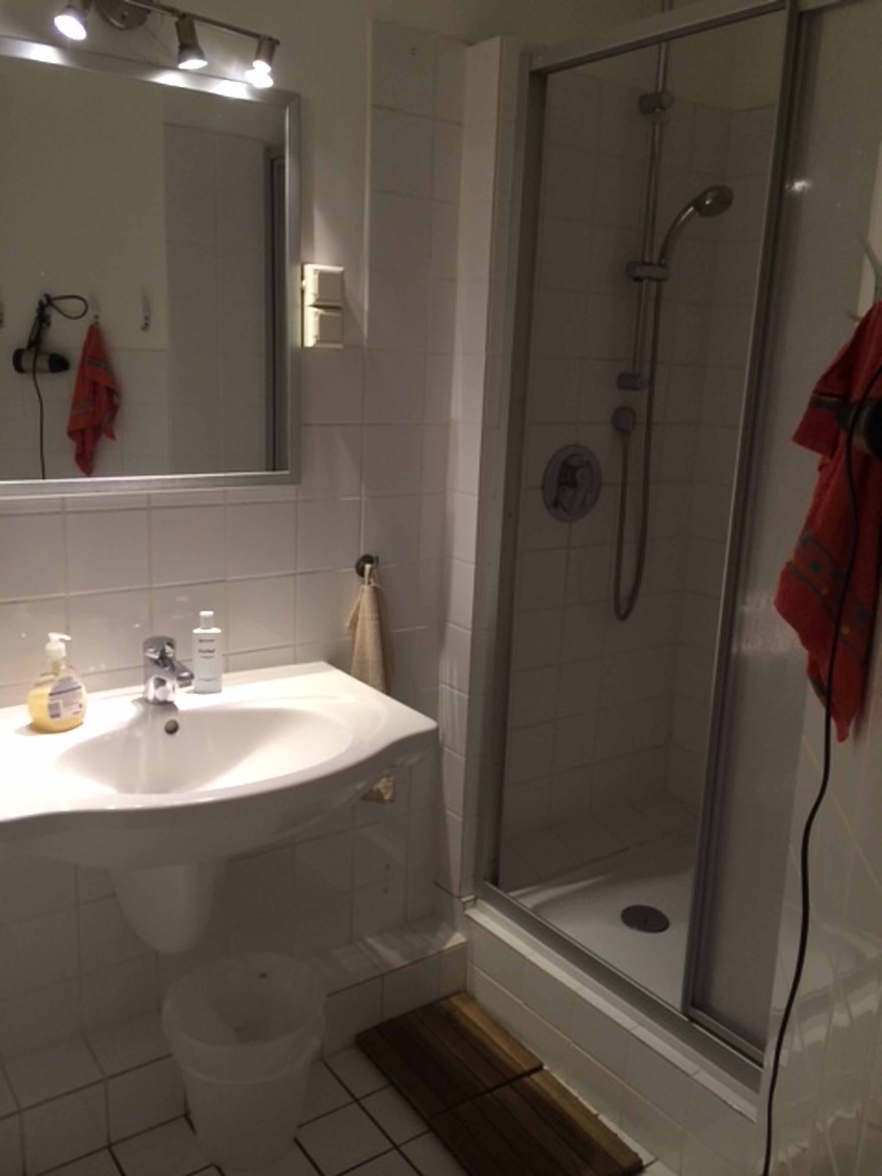 A bathroom with a white sink, a mirror, a shower with a glass door, and a towel hanging on the wall.