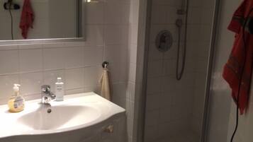 A bathroom with a white sink, a mirror, a shower with a glass door, and a towel hanging on the wall.