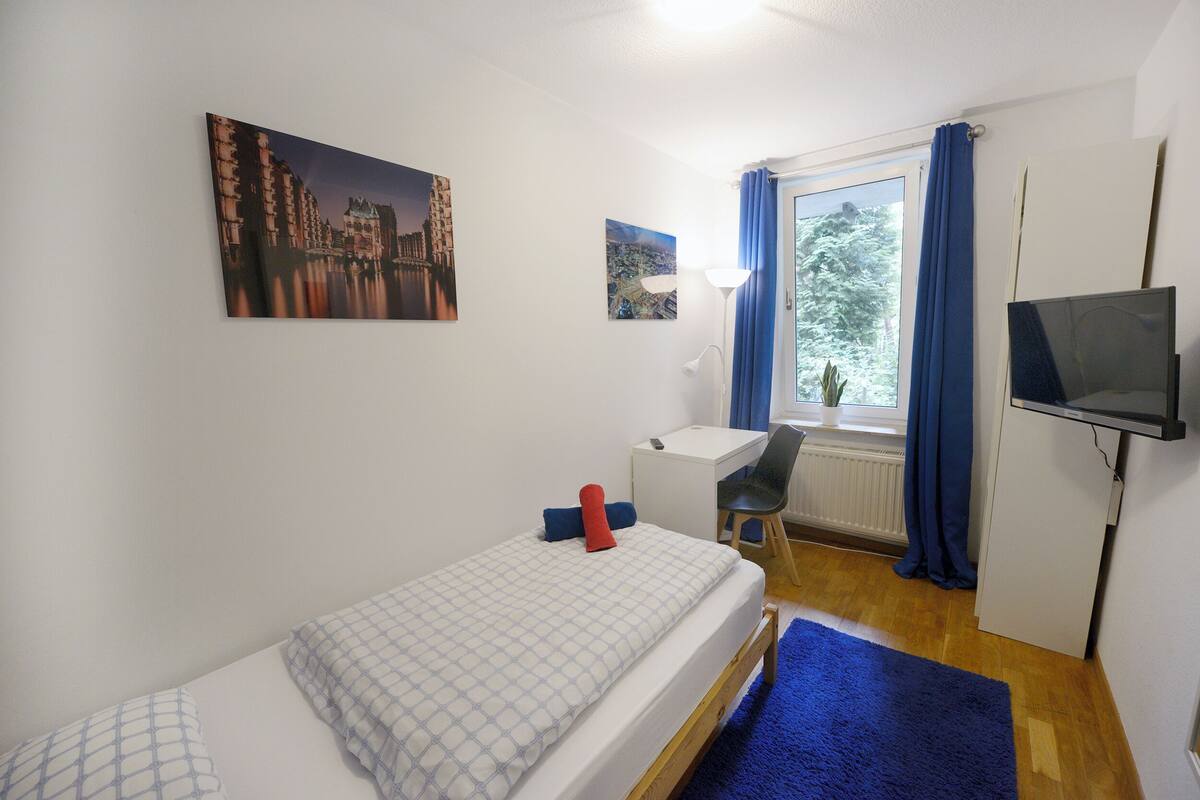 A small, tidy room with a bed, a desk, a chair, and a TV.