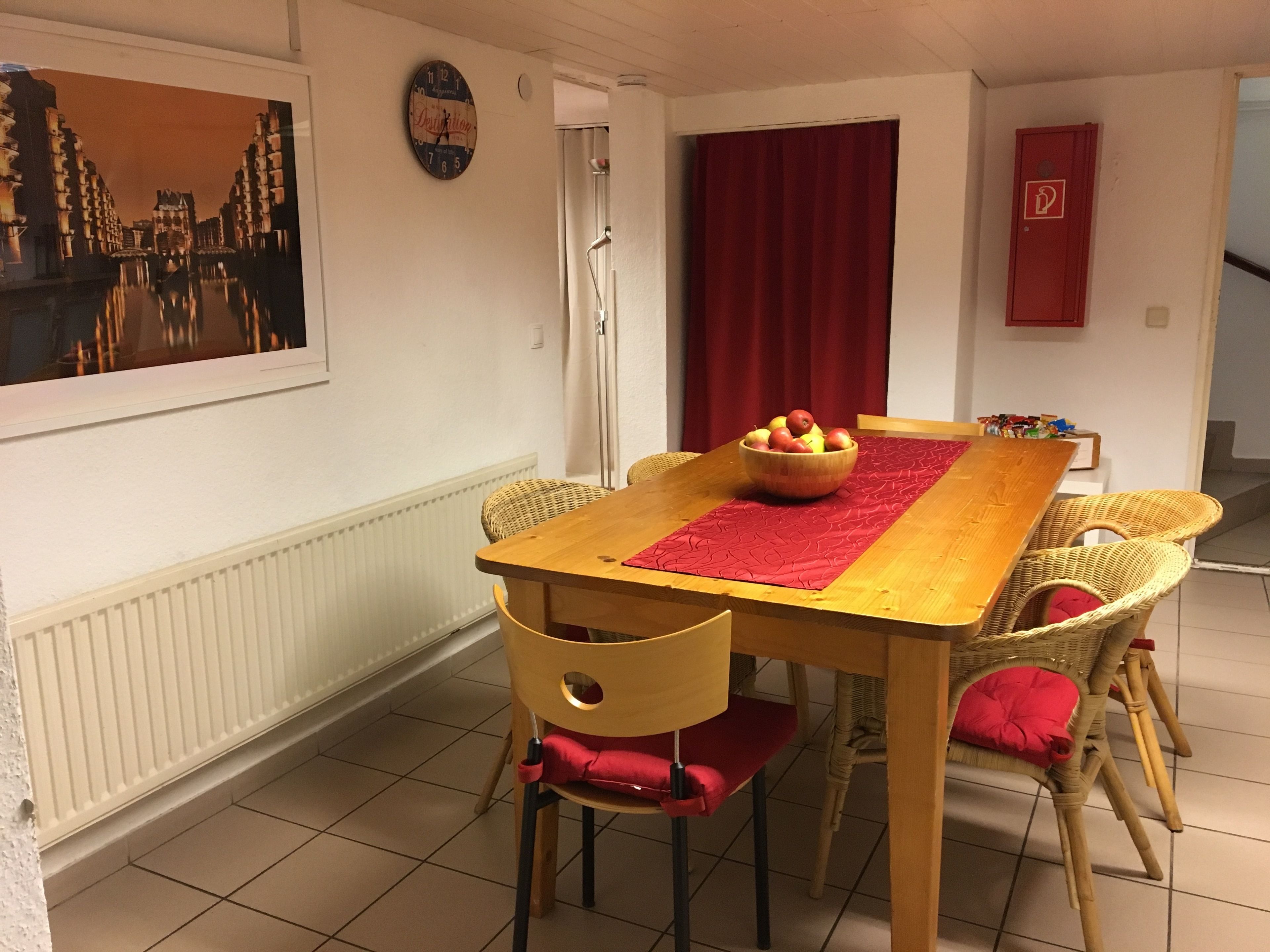 Ein Essbereich mit Holztisch, Korbstühlen, einer roten Tischläufer und einer Obstschale.