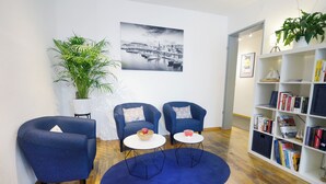 A modern living room with two blue armchairs, a coffee table, a bookshelf, and a large potted plant. - Basement Hamburg - Hostel (Hamburg)