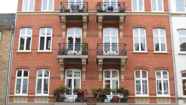 A multi-story building with a brick facade, multiple balconies with metal railings, and a central entrance with a tree. - Basement Hamburg - Hostel (Hamburg)