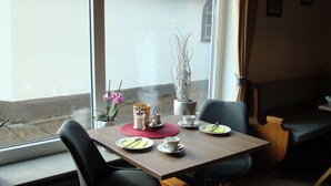 A dining area with a table set for two, chairs, a vase with flowers, and a view of the street outside. - Hotel Schindelberg (Oberstaufen)