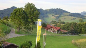 A rural landscape with a flag, a wooden fence, and a building with a red roof. - Hotel Schindelberg (Oberstaufen)