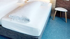 A double bed with white linens, a wooden headboard, and a blue carpeted floor. - Hotel Schindelberg (Oberstaufen)