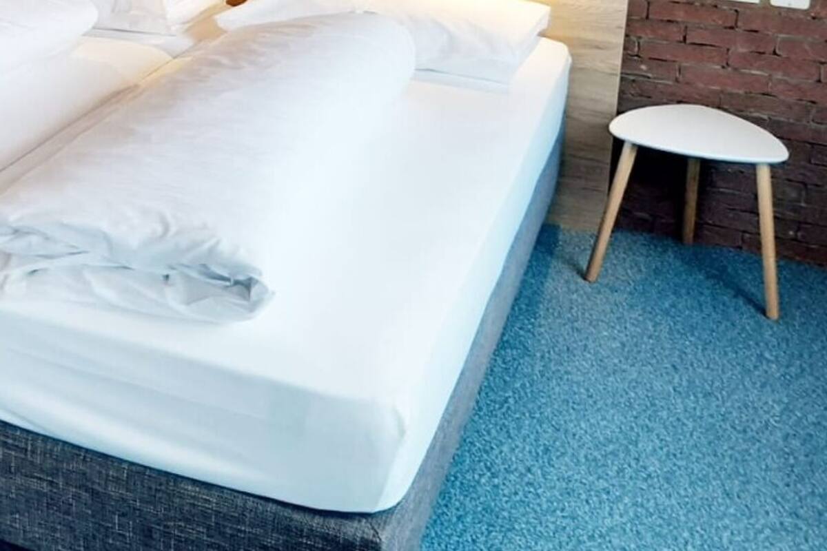 A double bed with white linens, a wooden headboard, and a blue carpeted floor.