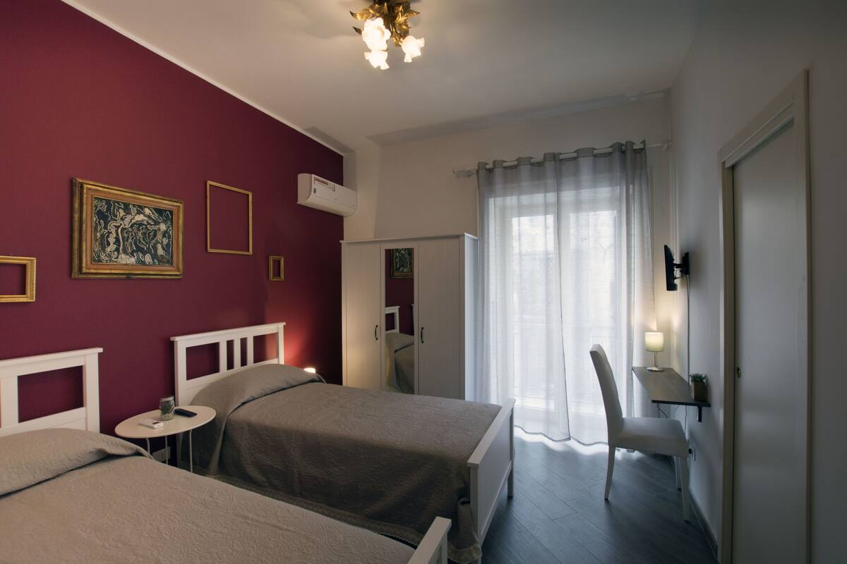 A hotel room with two beds, a desk, a chair, a mirror, and a window with curtains.