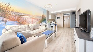 A modern living room with a sofa, a coffee table, and a TV. There is a kitchen area with a dining table and chairs. - Sun & Snow - Olympic Park (Kolobrzeg)
