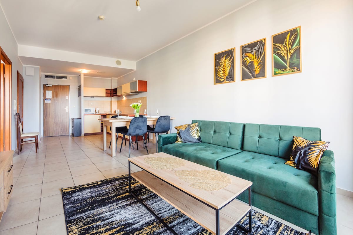 Ein modernes Wohnzimmer mit einem grünen Sofa, einem Holztisch und einem Essbereich mit Stühlen und einem Tisch.