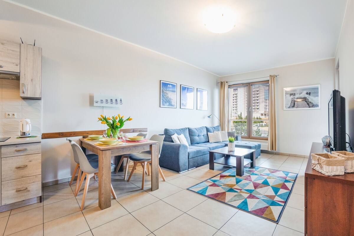 Eine moderne Wohnung mit Küche, Essbereich und Wohnzimmer. Sie verfügt über ein blaues Sofa, einen Couchtisch und einen farbenfrohen Teppich.