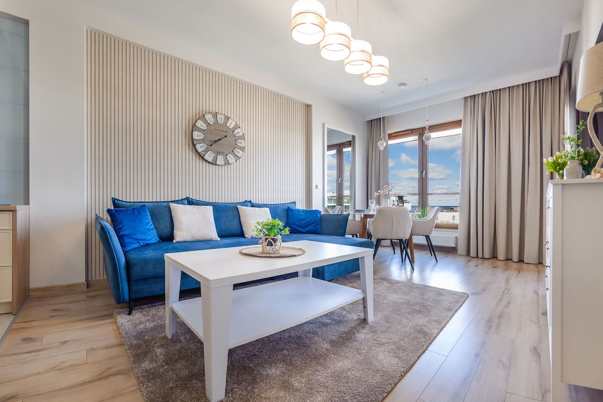 Ein modernes Wohnzimmer mit einem blauen Sofa, einem weißen Couchtisch und einer großen Wanduhr.