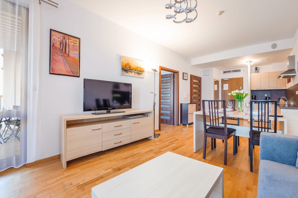 Ein modernes Wohnzimmer mit Flachbildfernseher, Holzmöbeln und einem Essbereich mit Tisch und Stühlen.