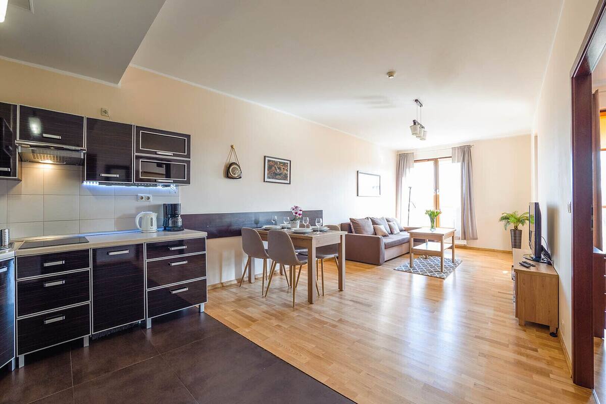 Eine moderne Küche mit dunklen Schränken und einem Essbereich mit einer Couch und einem Tisch.