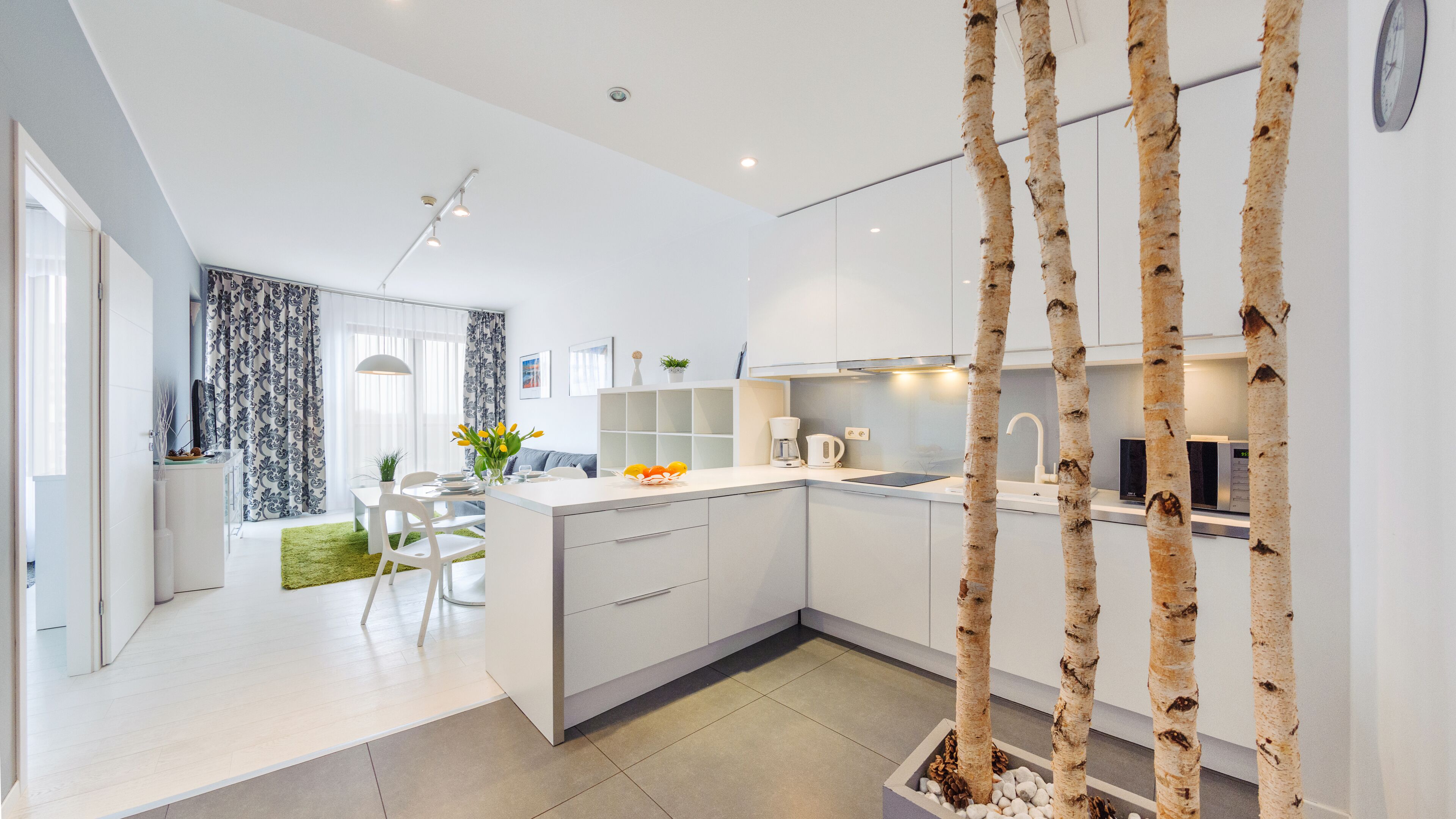 Een moderne keuken met witte kasten, een centraal eiland en een eetgedeelte met een witte tafel en stoelen.