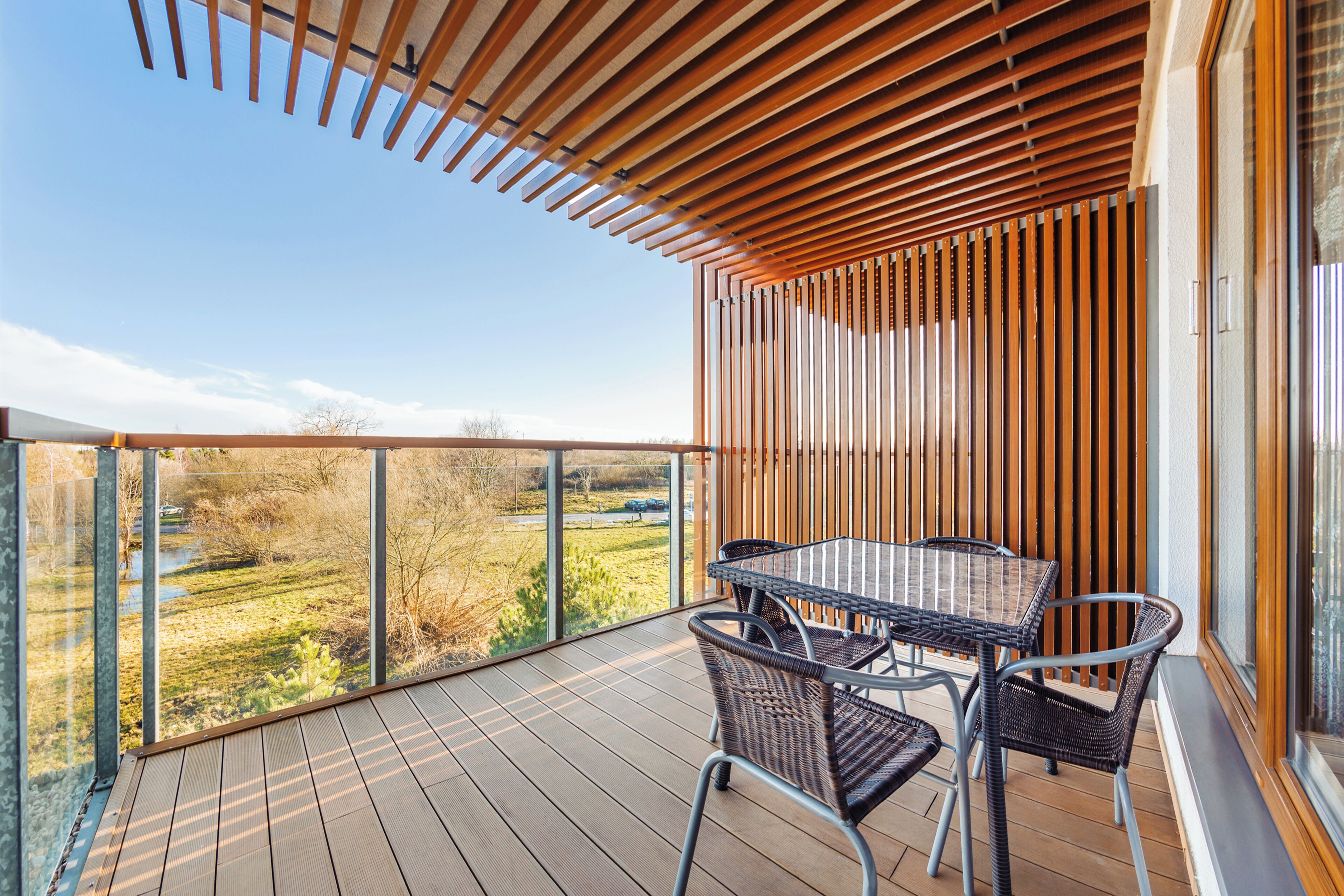 A wooden deck with a glass balustrade, wicker furniture, and a view of a field.