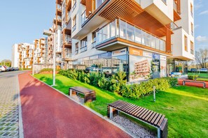 Un moderno edificio de apartamentos con balcones, una ciclovía roja y jardines verdes.