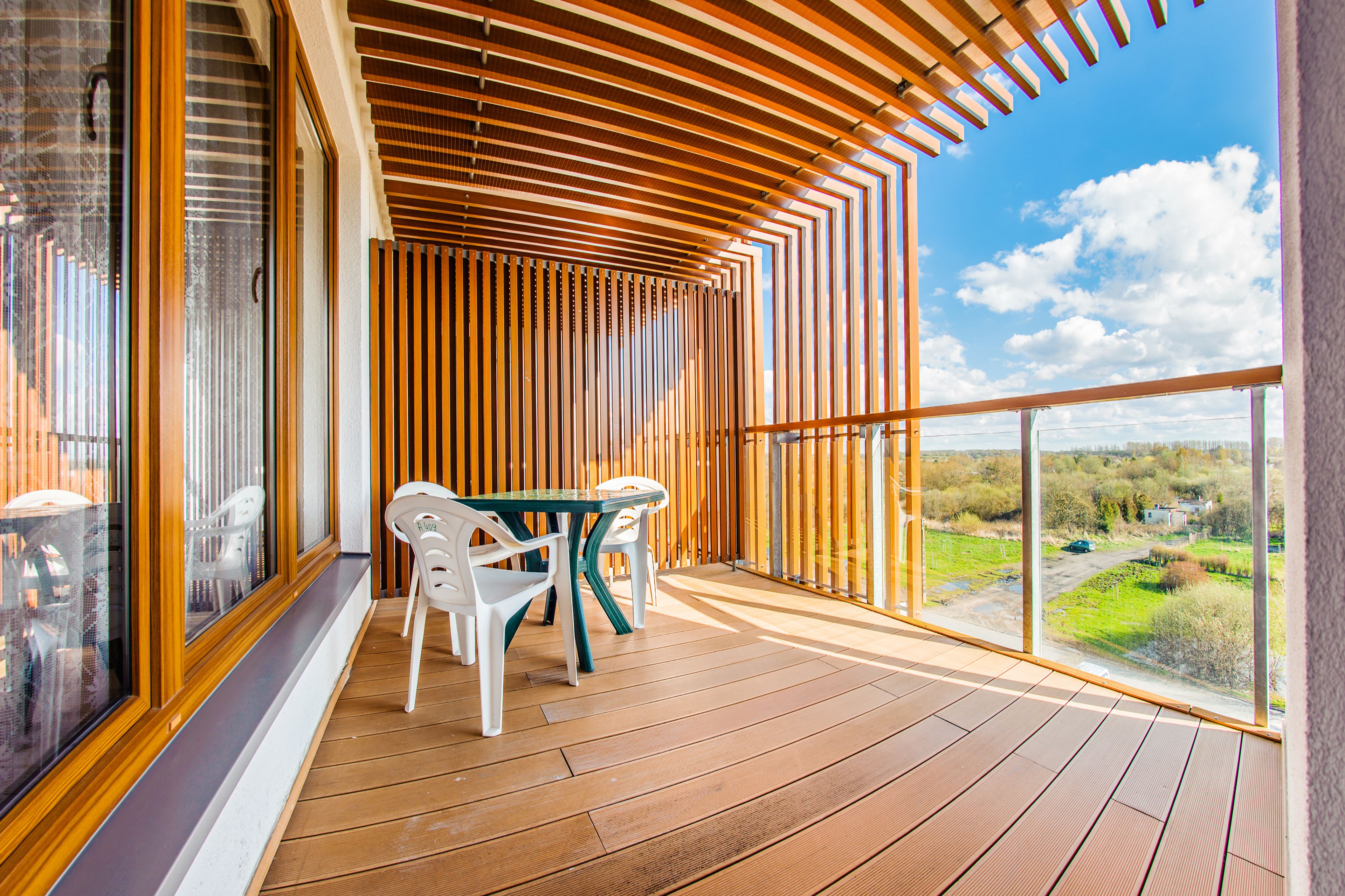 A wooden deck with a table and chairs, large windows, and a view of the countryside.