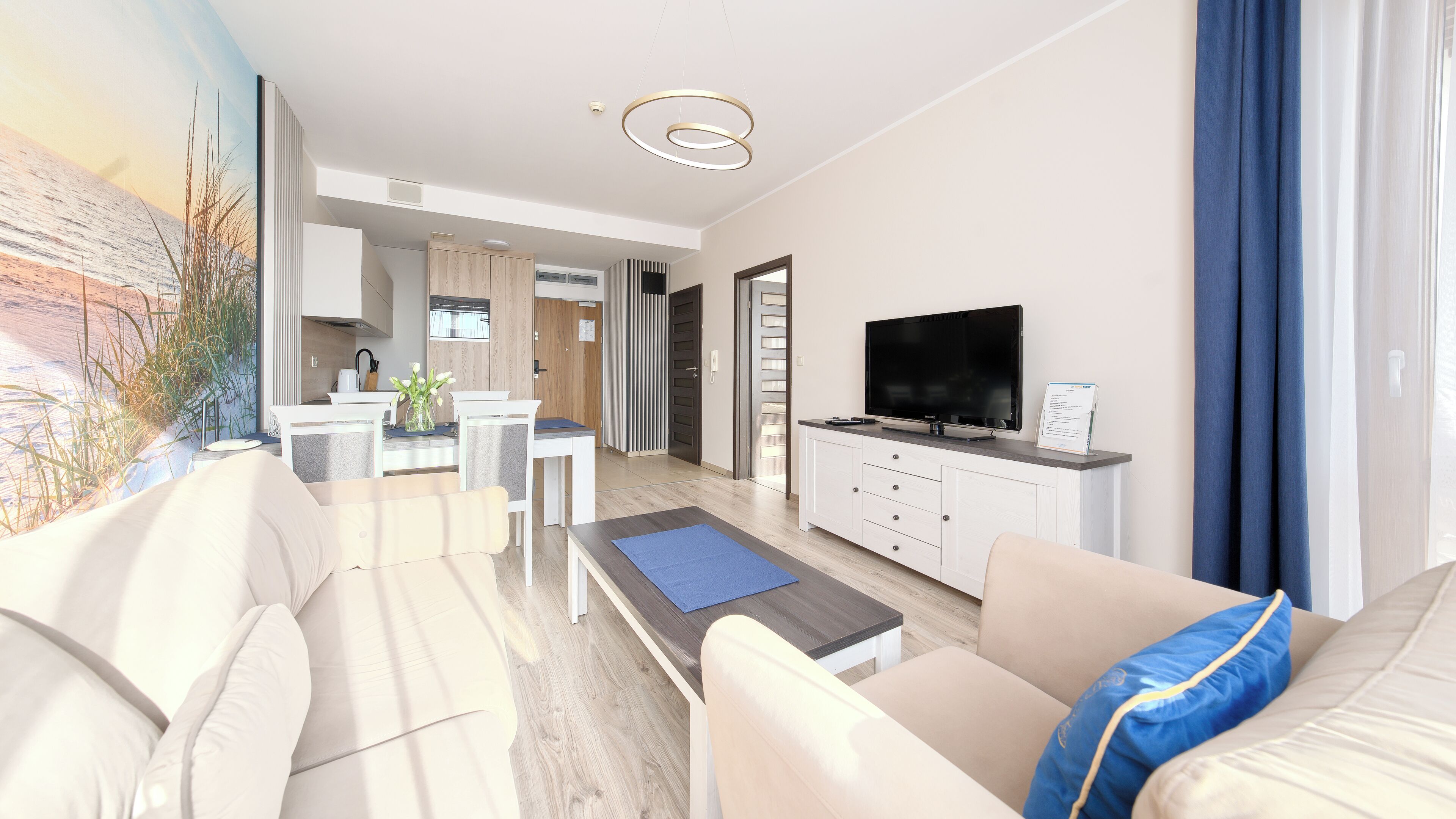 Una sala de estar moderna con un sofá, una mesa de centro y un televisor. Hay una zona de cocina con una mesa de comedor y sillas.