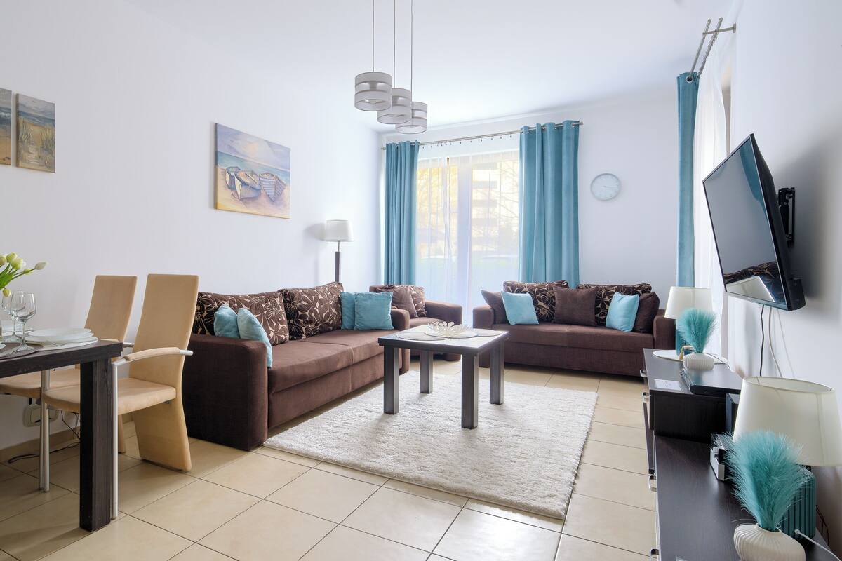 Ein Wohnzimmer mit einer Couch, Sesseln, einem Couchtisch, einem Fernseher und Kunstwerken an der Wand.