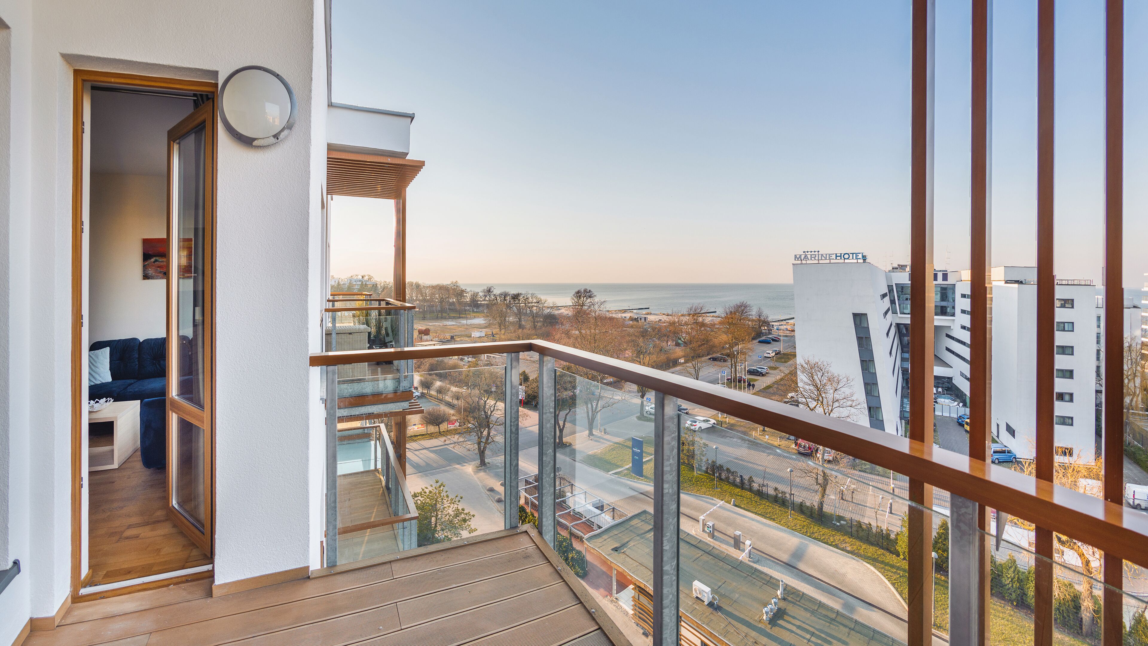Un balcon avec vue sur la mer et la ville, un plancher en bois et une rambarde en verre.