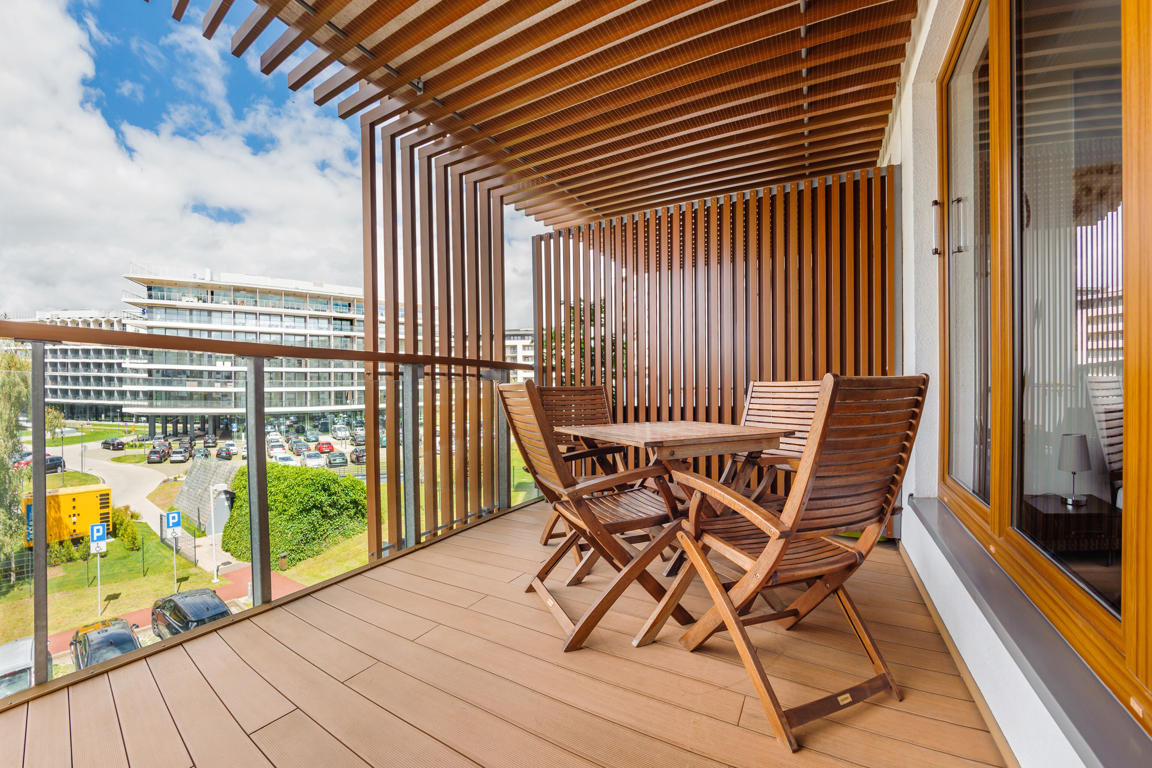 Ein Balkon mit Holztisch und Stühlen, mit Blick auf einen Parkplatz und Gebäude.
