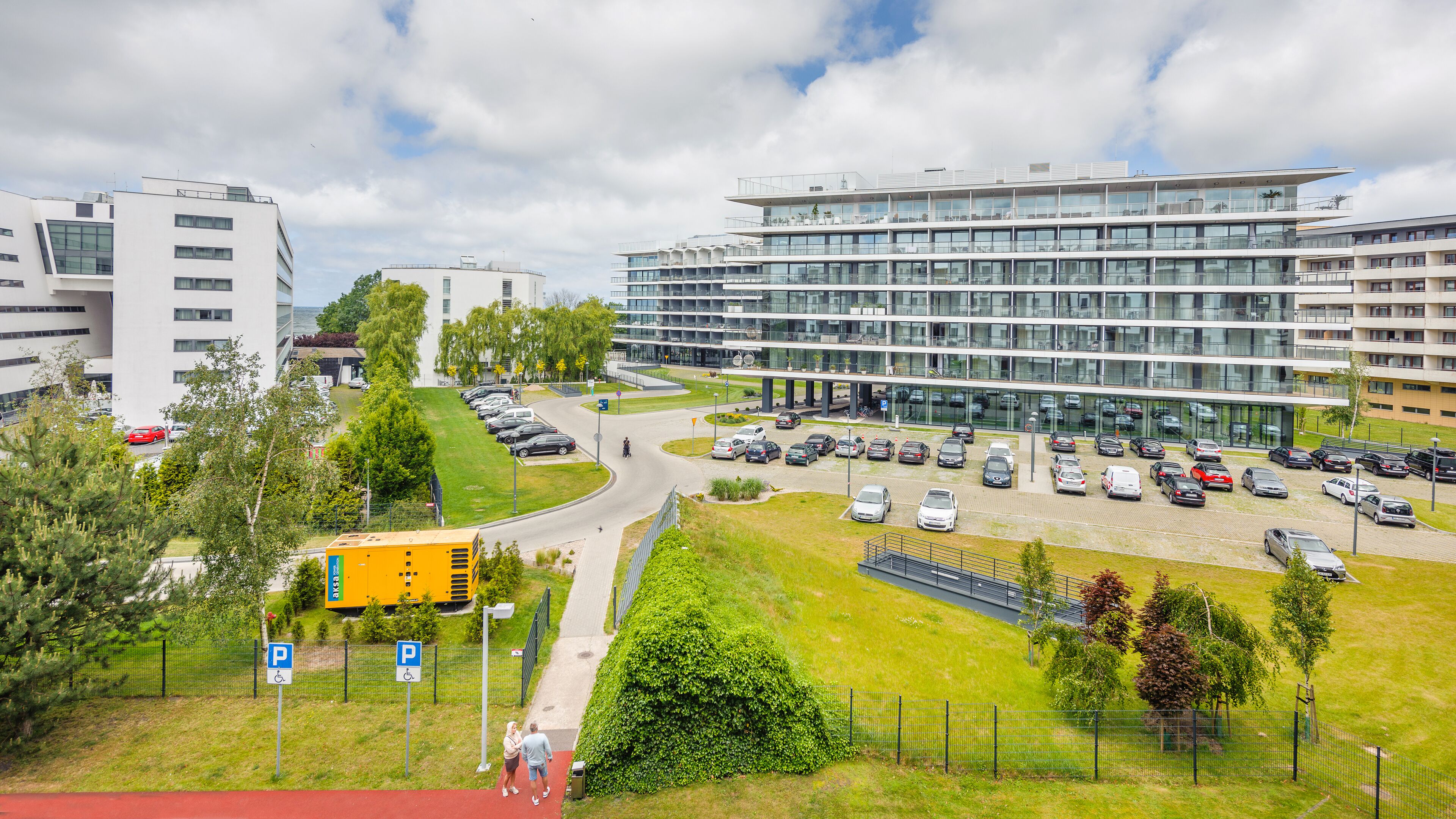En modern byggnad med flera våningar, en parkeringsplats och ett grönområde med en gångstig.