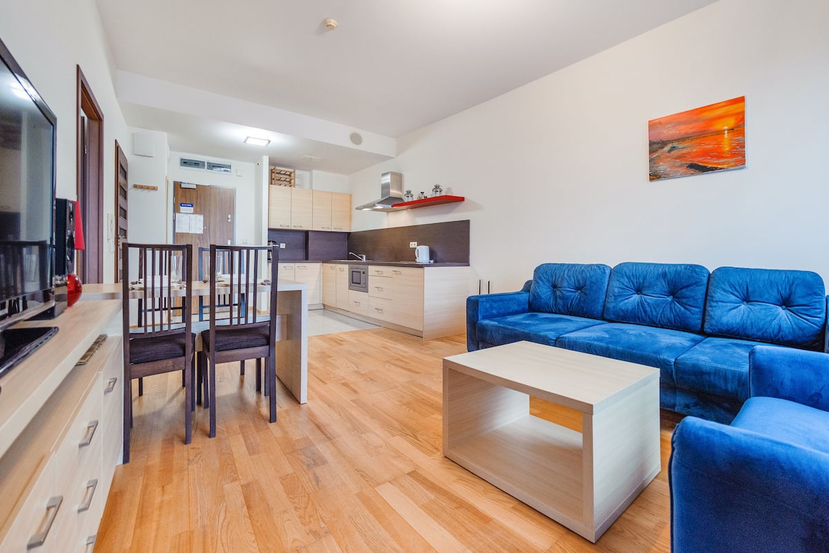 Ein modernes Wohnzimmer mit einem blauen Sofa, einem Holztisch und einem Essbereich mit Stühlen und Tisch.