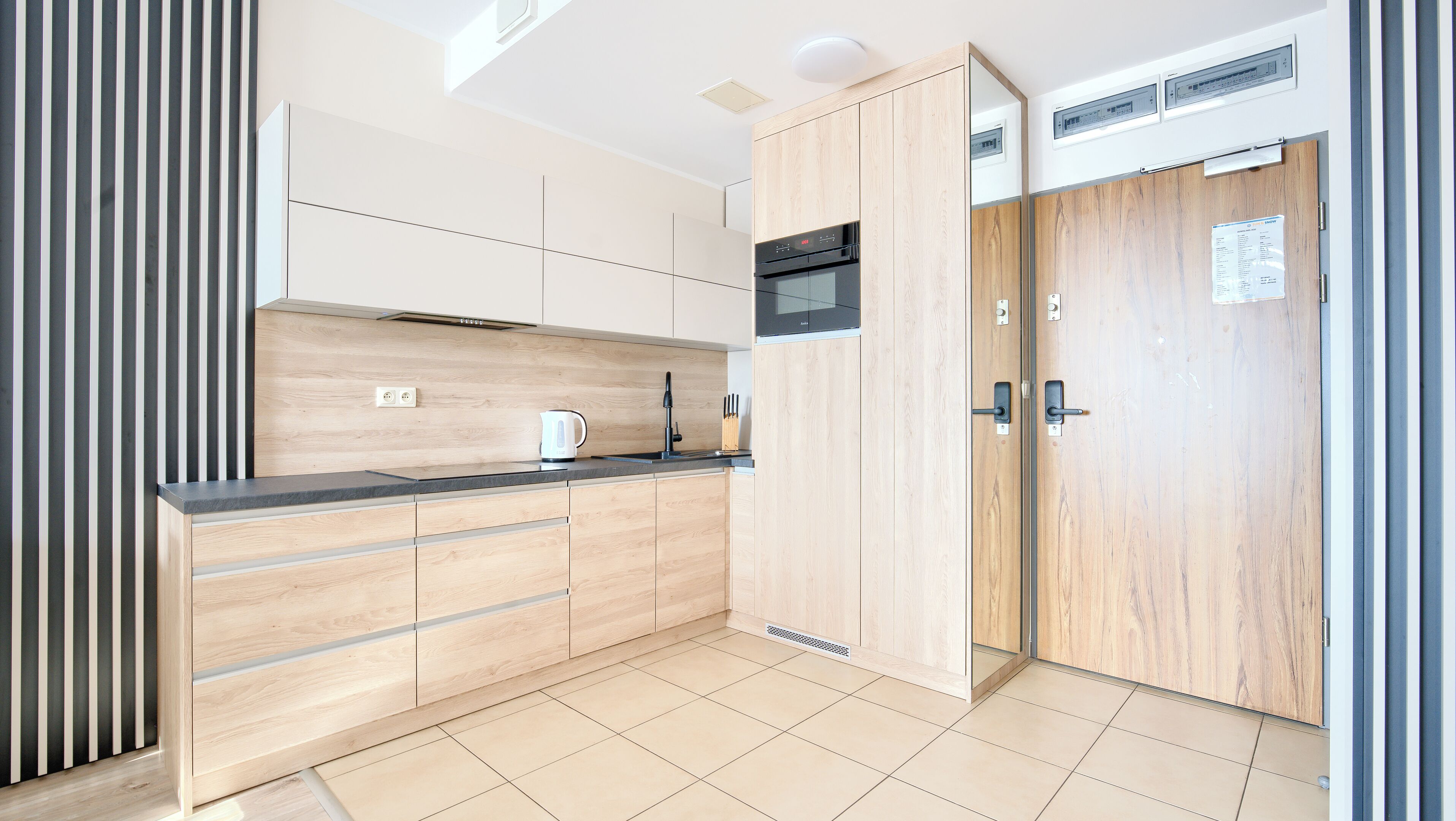 A modern kitchen with wooden cabinets, a black microwave, and a kettle on the counter.
