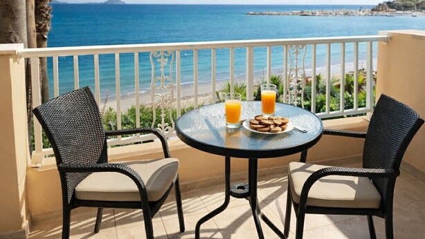 A balcony with two wicker chairs, a round table, and a view of the sea. - Nel Mare Studios (Zakynthos)