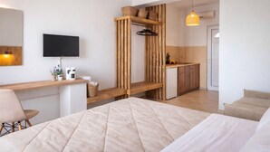 A modern hotel room with a bed, a TV, a wooden shelf with baskets, a kitchen area, and a hanging light fixture. - Nel Mare Studios (Zakynthos)