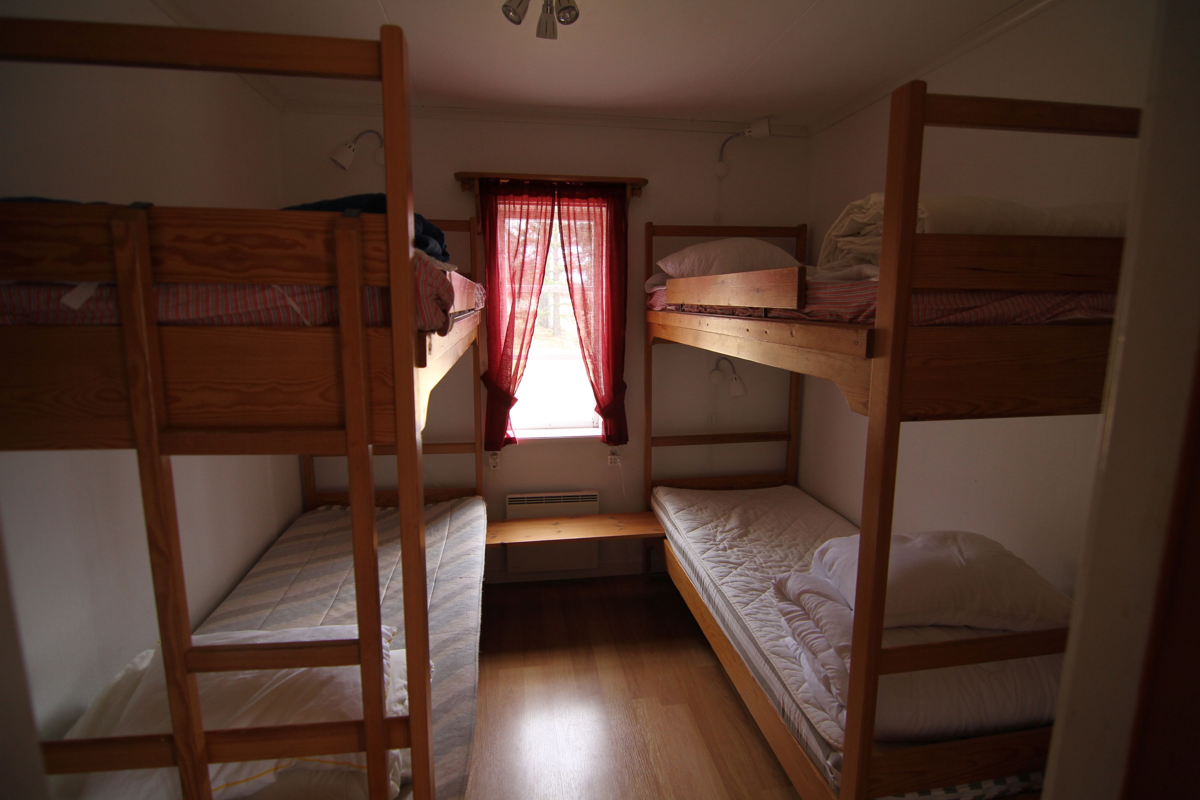 Un dormitorio con literas, una ventana con cortinas rojas y un ventilador de techo.