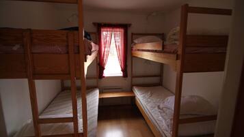 Un dormitorio con literas, una ventana con cortinas rojas y un ventilador de techo.