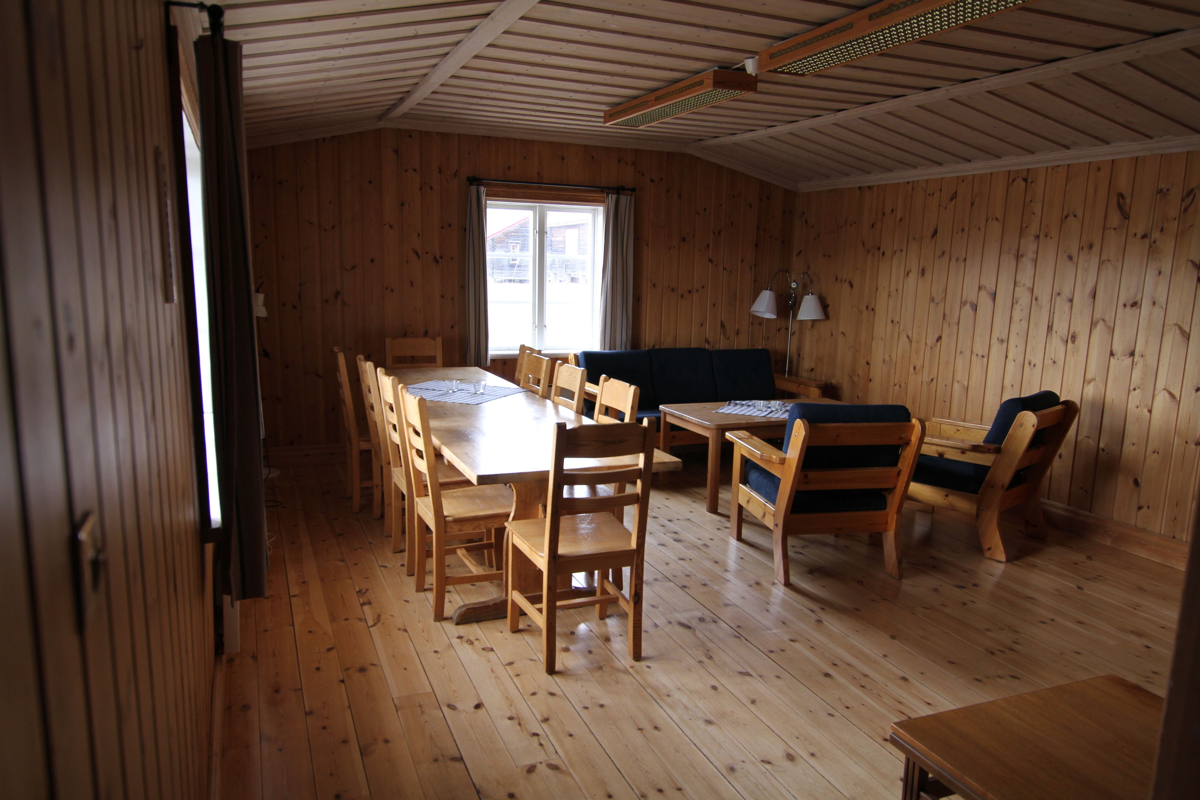 A wooden-paneled room with a dining table, chairs, a sofa, and a window.