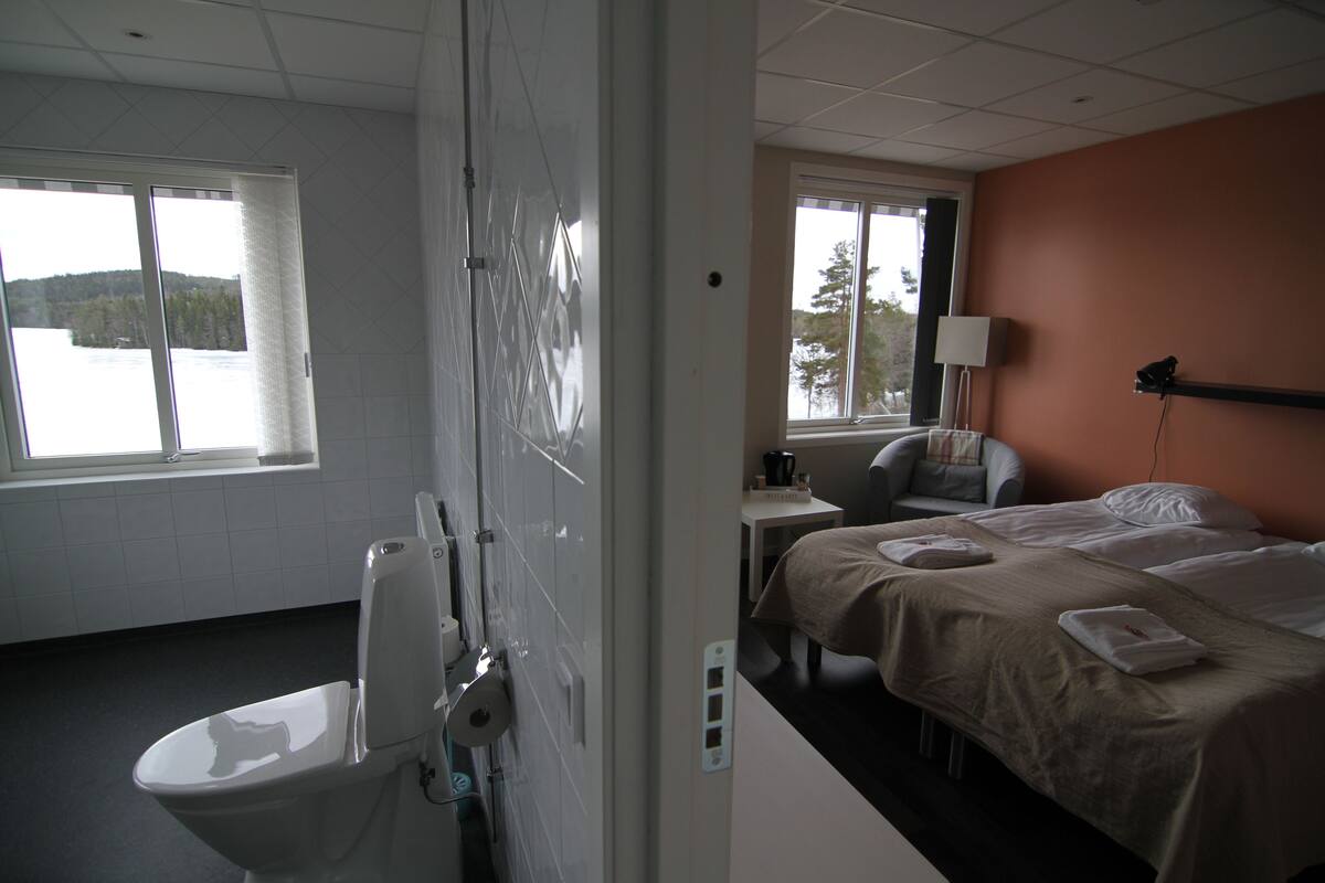A hotel room with a bed, a chair, a desk, and a view of a lake through the window.