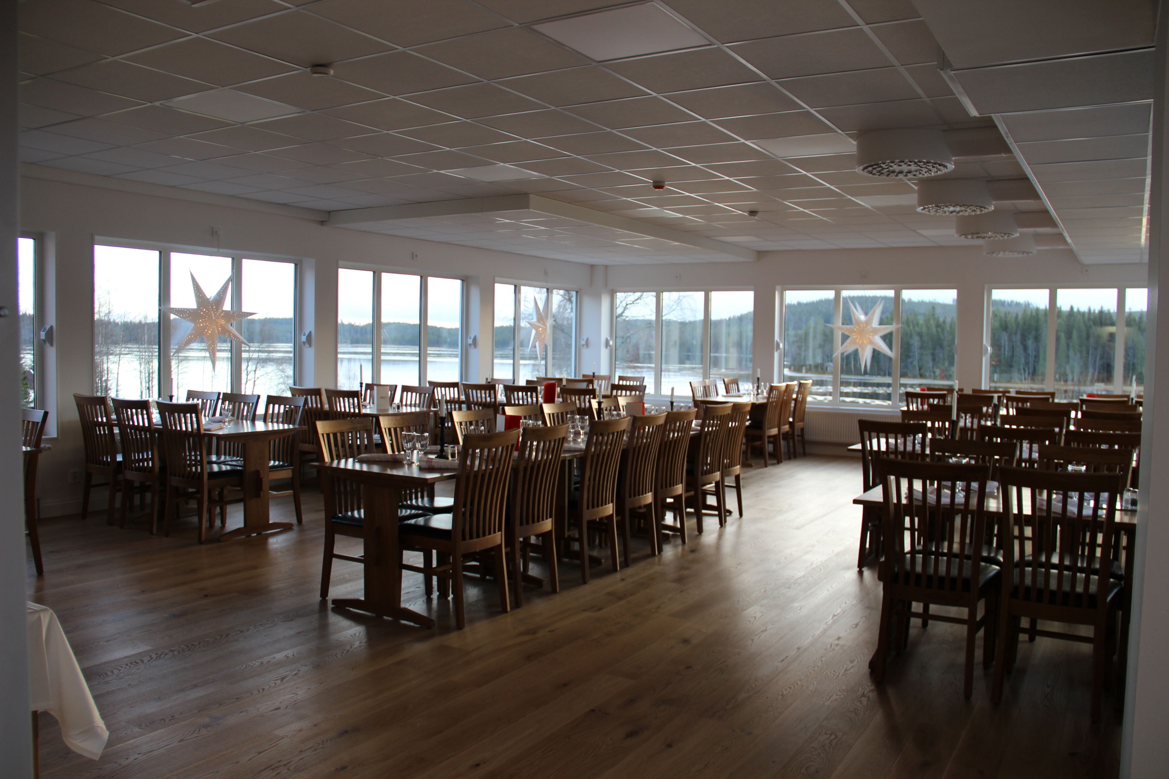 A spacious dining area with wooden tables and chairs, large windows offering a view of a lake and forest, and a star decoration on the ceiling.