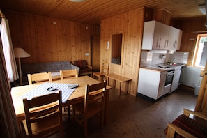 A wooden cabin with a dining table, chairs, a sofa, and a kitchenette. - Harsa B&B, Stugby & Vandrarhem (Jarvso)