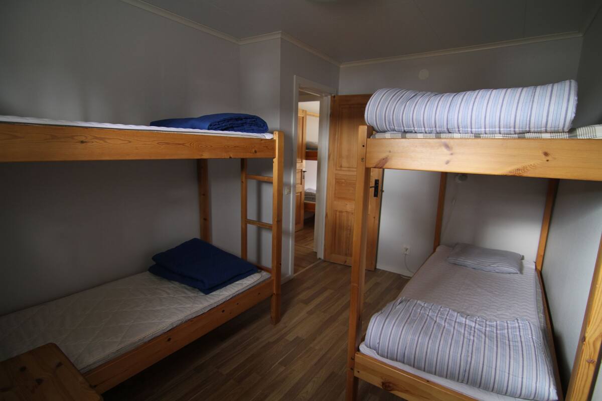 A room with two bunk beds, wooden flooring, and a door leading to another room.