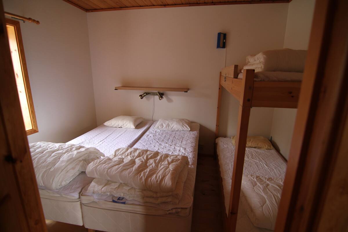A dormitory room with two bunk beds, a wooden shelf, and a small window.