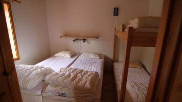 Ein Schlafsaalzimmer mit zwei Etagenbetten, einem Holzregal und einem kleinen Fenster.