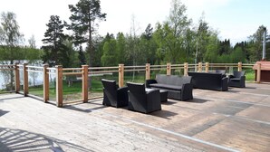 Une terrasse extérieure avec un plancher en bois, des meubles en osier et une rambarde en bois.