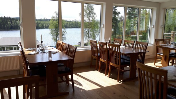 Un espace repas avec des tables et des chaises en bois, de grandes fenêtres offrant une vue sur un lac et une forêt.