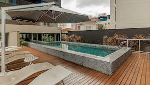 Un área de piscina en la azotea con sillones y una zona de estar cubierta.