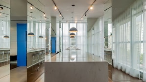 Un hall de hotel moderno con mostrador de recepción de mármol, divisiones de vidrio y ventanas amplias con cortinas traslúcidas.