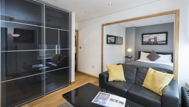 Une chambre d’hôtel moderne dotée d’un grand lit, d’un canapé en cuir, d’une cloison en verre et offrant une vue sur le paysage urbain.