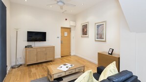 Un salon moderne doté d’un téléviseur à écran plat, de meubles en bois, d’un ventilateur de plafond et d’œuvres d’art accrochées aux murs.