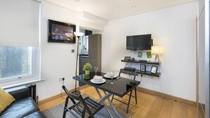 Un espace de vie moderne et compact comprenant un coin repas, un canapé, un téléviseur et une petite cuisine.