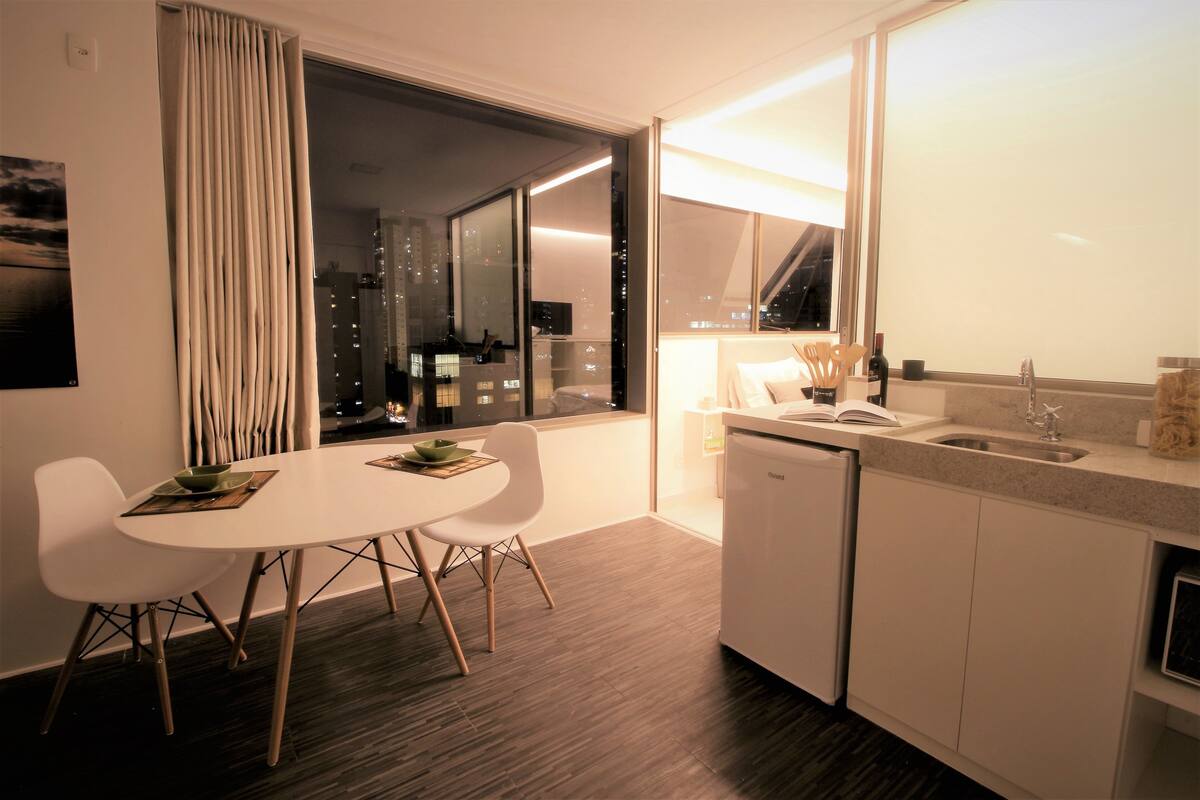 A modern kitchen with a dining area, featuring a large window, white cabinetry, and a built-in dishwasher.