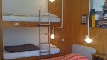 A bunk bed room with a ladder, a small table, and a colorful striped bedspread.