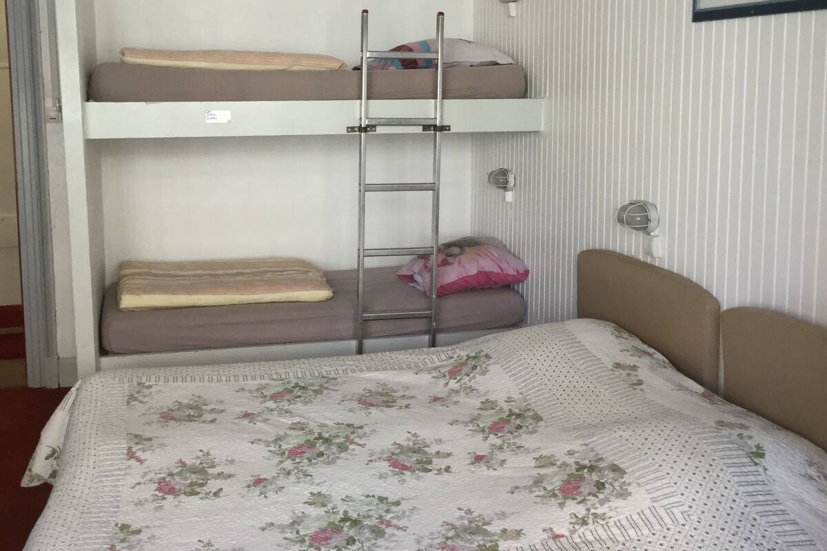 Een slaapkamer met een stapelbed en een ladder, een ingelijste foto aan de muur, en een sprei met bloemenprint.